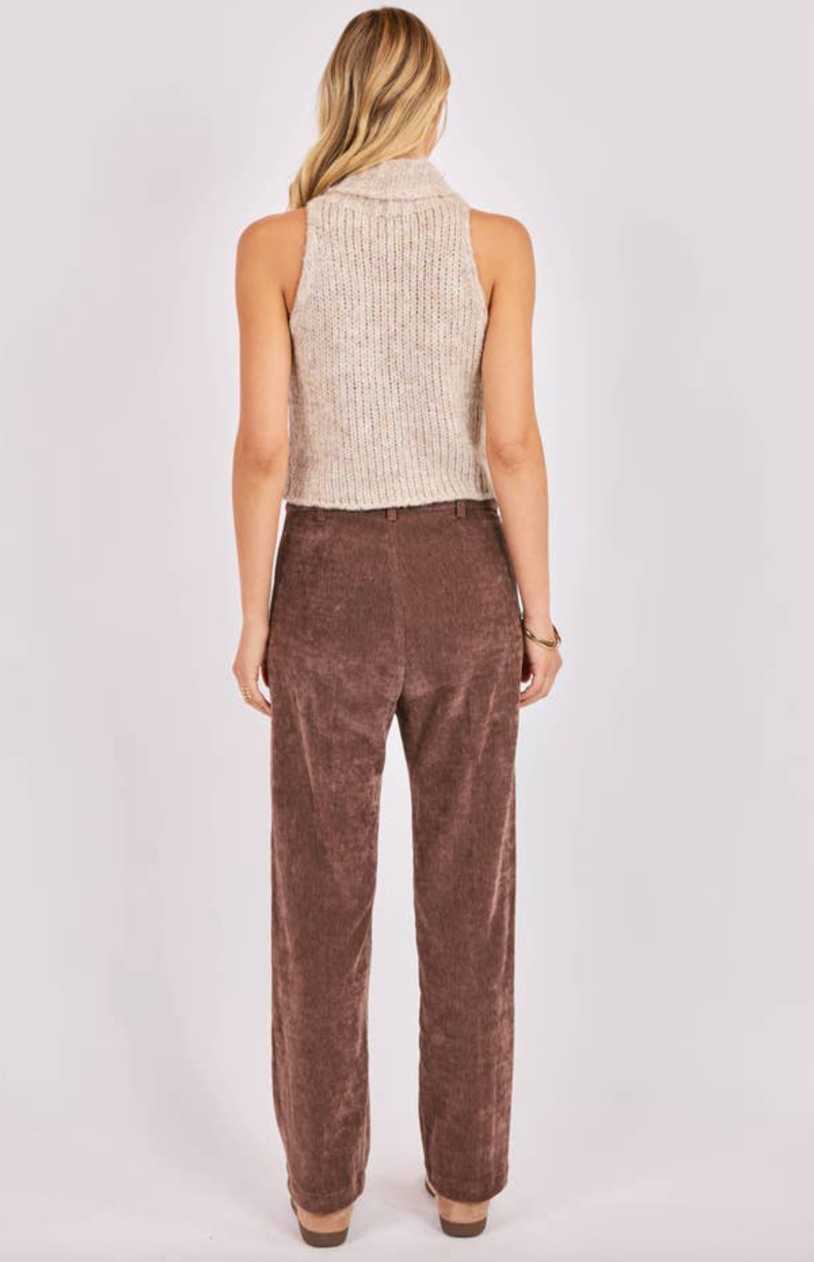 Woman wearing a beige sleeveless sweater and brown pants on a white background