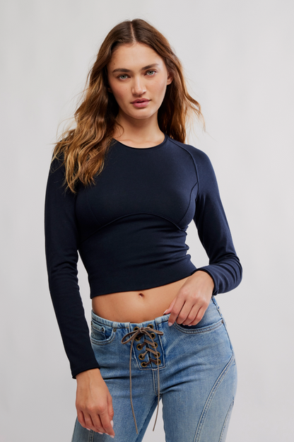 Woman wearing a black long-sleeve crop top and blue jeans against a plain background