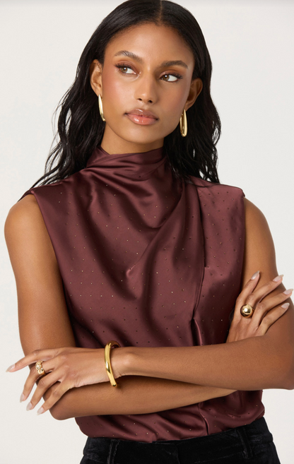 Woman wearing sleeveless satin cowl neck top in deep brown with gold jewelry and subtle back-tie detail.