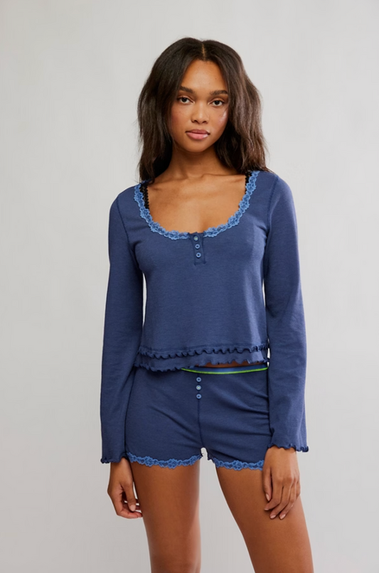 Woman wearing a blue pajama set with lace trim on a plain background