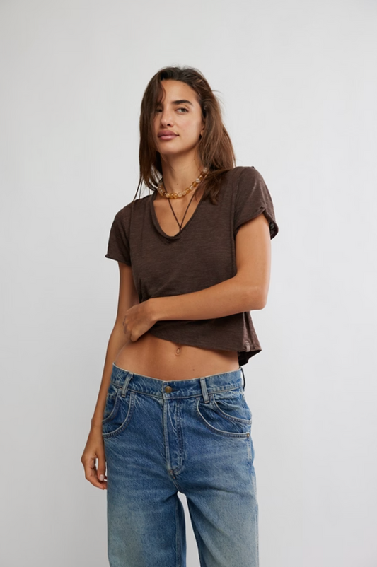 Woman wearing a brown crop top and blue jeans against a plain background