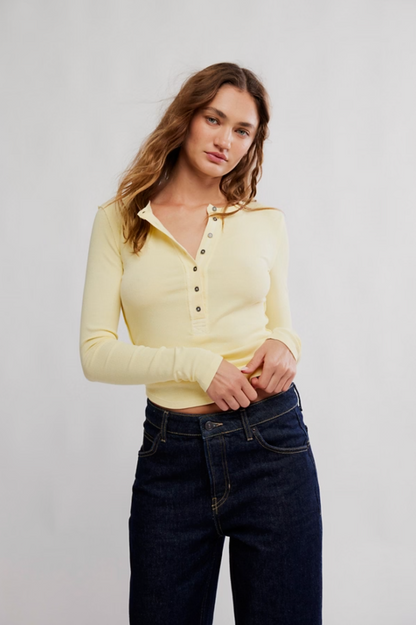Woman wearing a yellow long-sleeve polo shirt and dark jeans against a plain background
