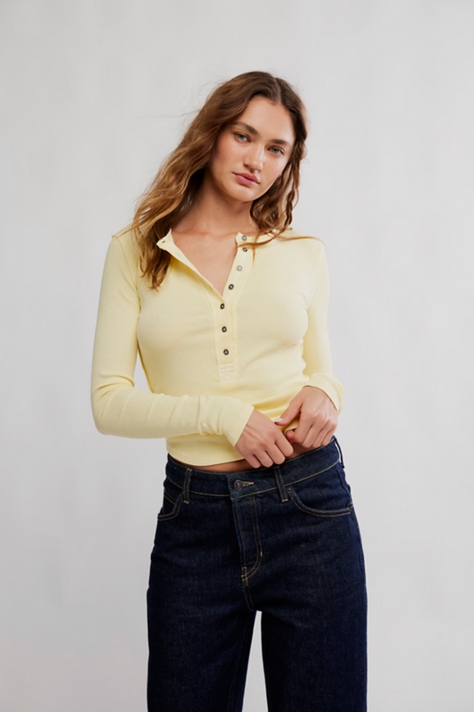 Woman wearing a yellow long-sleeve polo shirt and dark jeans against a plain background