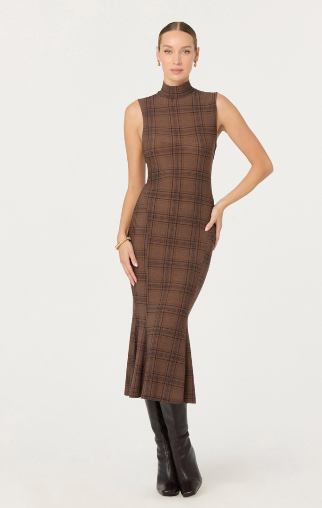 Woman wearing a brown plaid dress with black boots on a white background