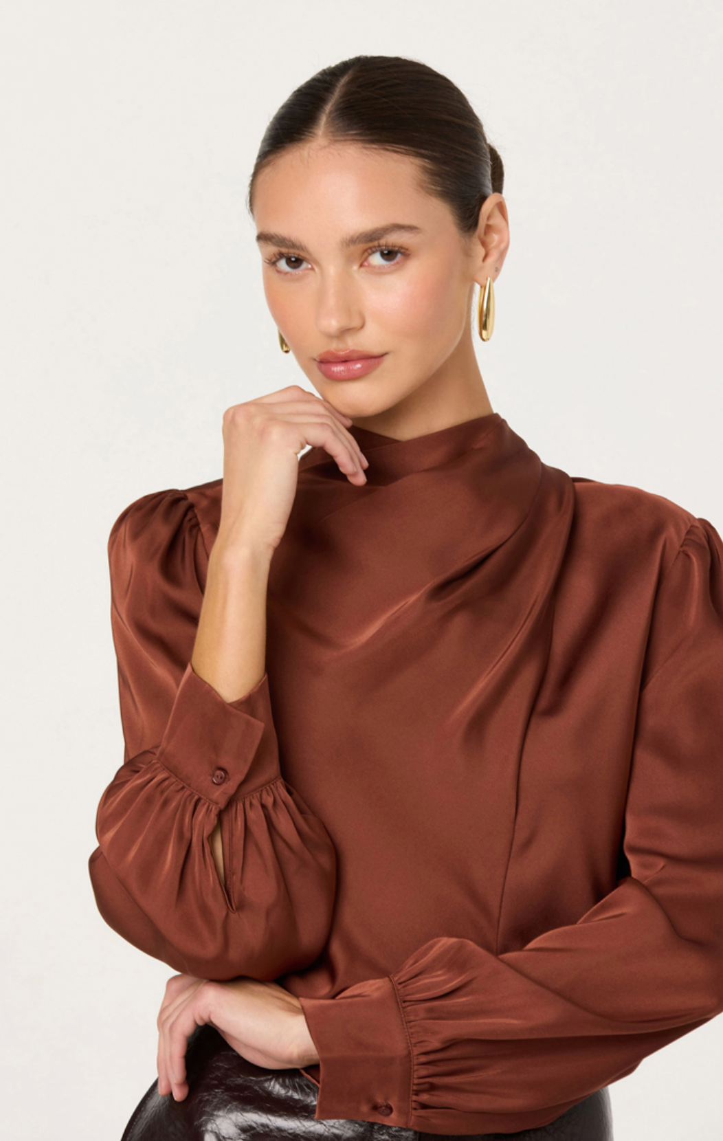 Woman wearing a brown blouse with puffed sleeves against a plain background