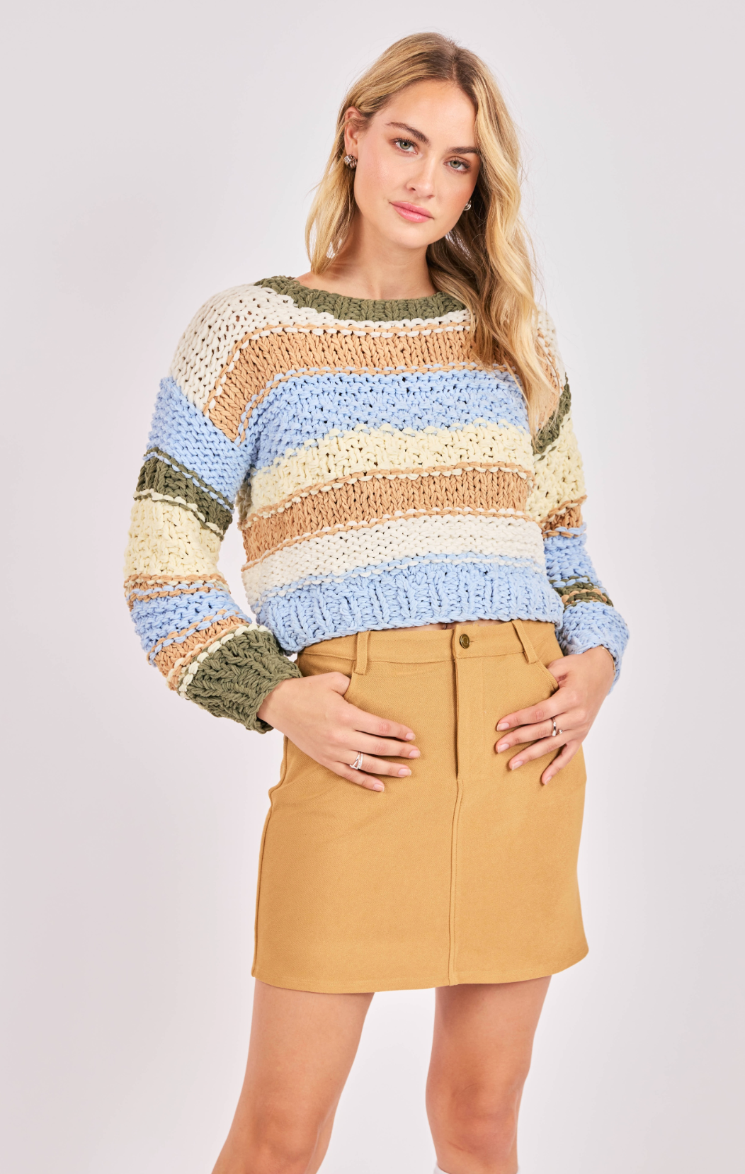 Woman wearing a multicolored striped sweater and beige skirt on a white background