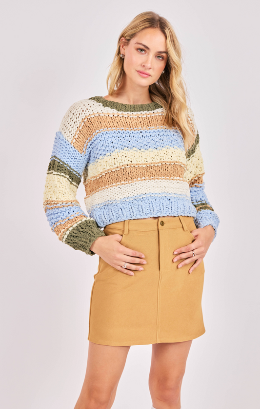 Woman wearing a multicolored striped sweater and beige skirt on a white background