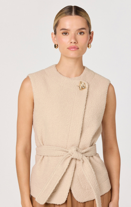 Woman wearing a beige sleeveless top with a brooch on a white background