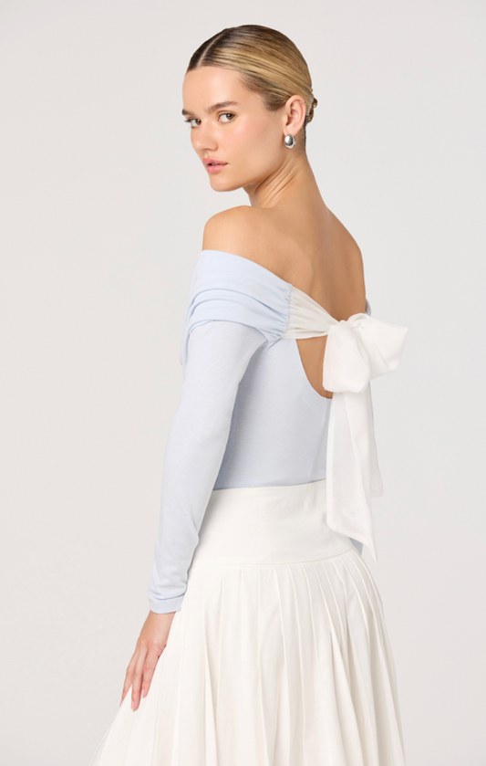 Woman wearing a light blue off-shoulder top with a white bow detail on a plain background
