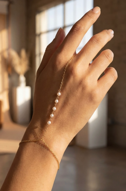 Hand wearing a delicate gold bracelet with pearls against a blurred indoor background