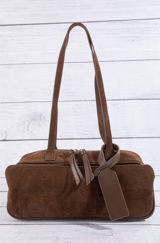 Brown suede handbag with a strap on a light wooden surface