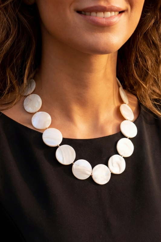 Close-up of a woman wearing a white beaded necklace against a black background