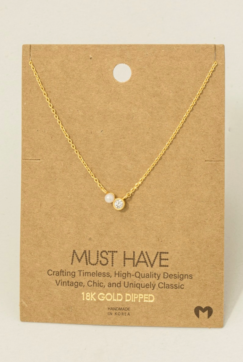 Gold necklace with two small round stones on a brown card with text