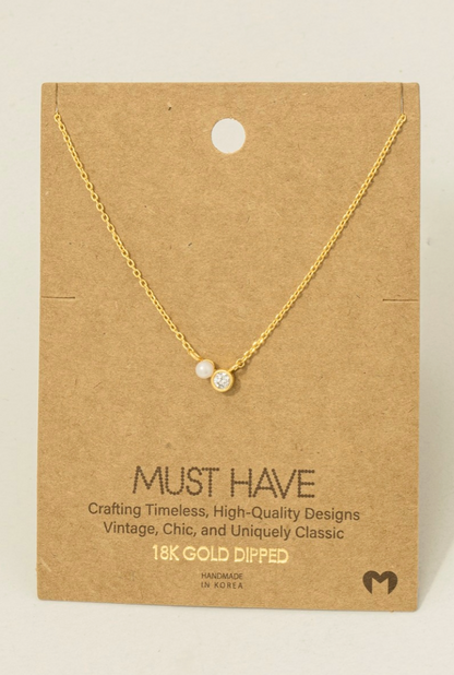 Gold necklace with two small round stones on a brown card with text