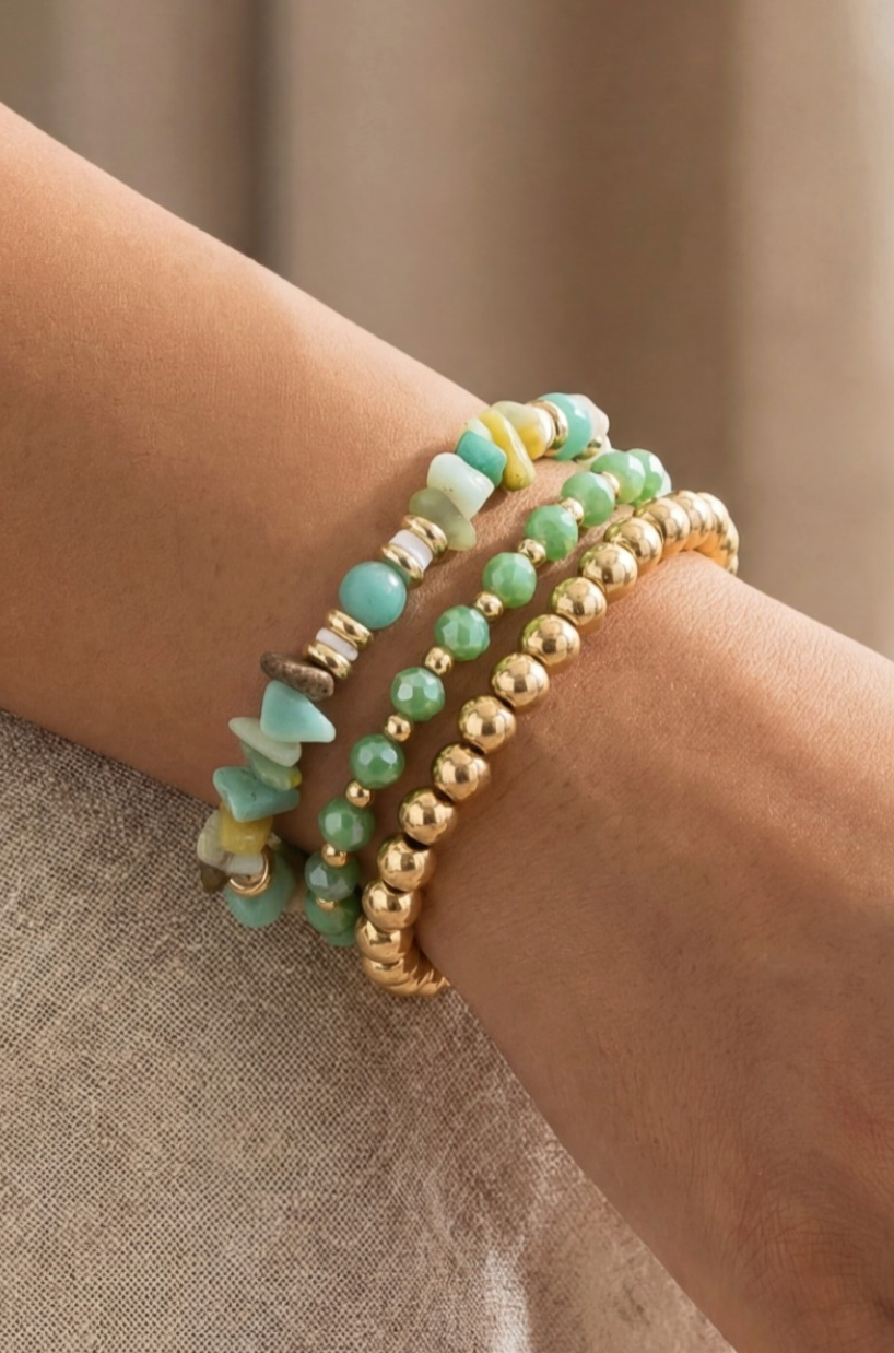 Stack of green and gold beaded bracelets on a wrist against a neutral background