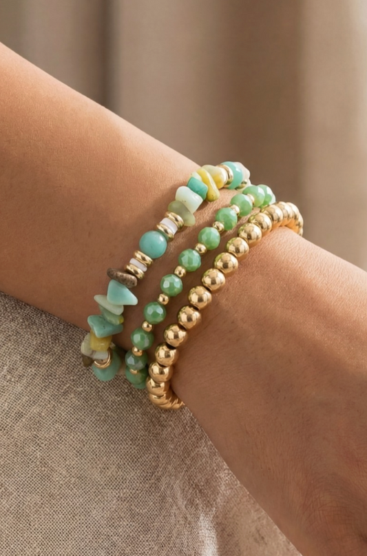 Stack of green and gold beaded bracelets on a wrist against a neutral background