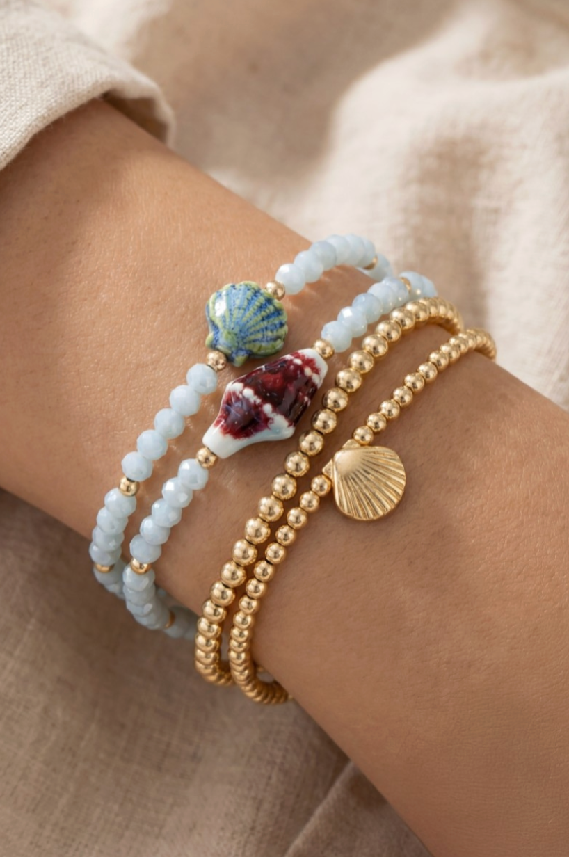 Bracelets with shell and bead designs on a wrist against a beige background
