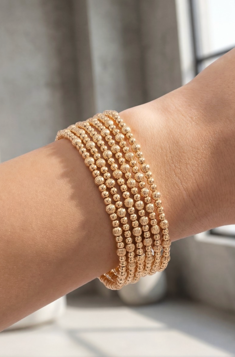 Gold beaded bracelet on a wrist with a neutral background