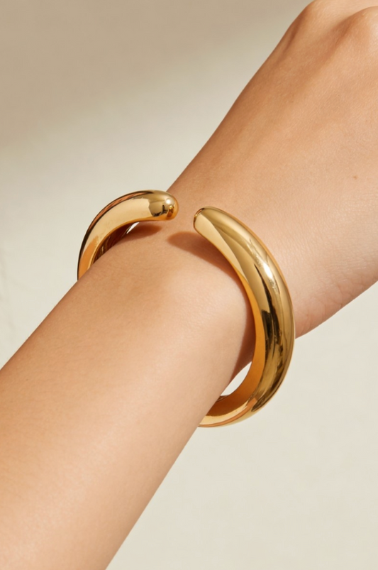 Gold bangles on a person's wrist against a neutral background