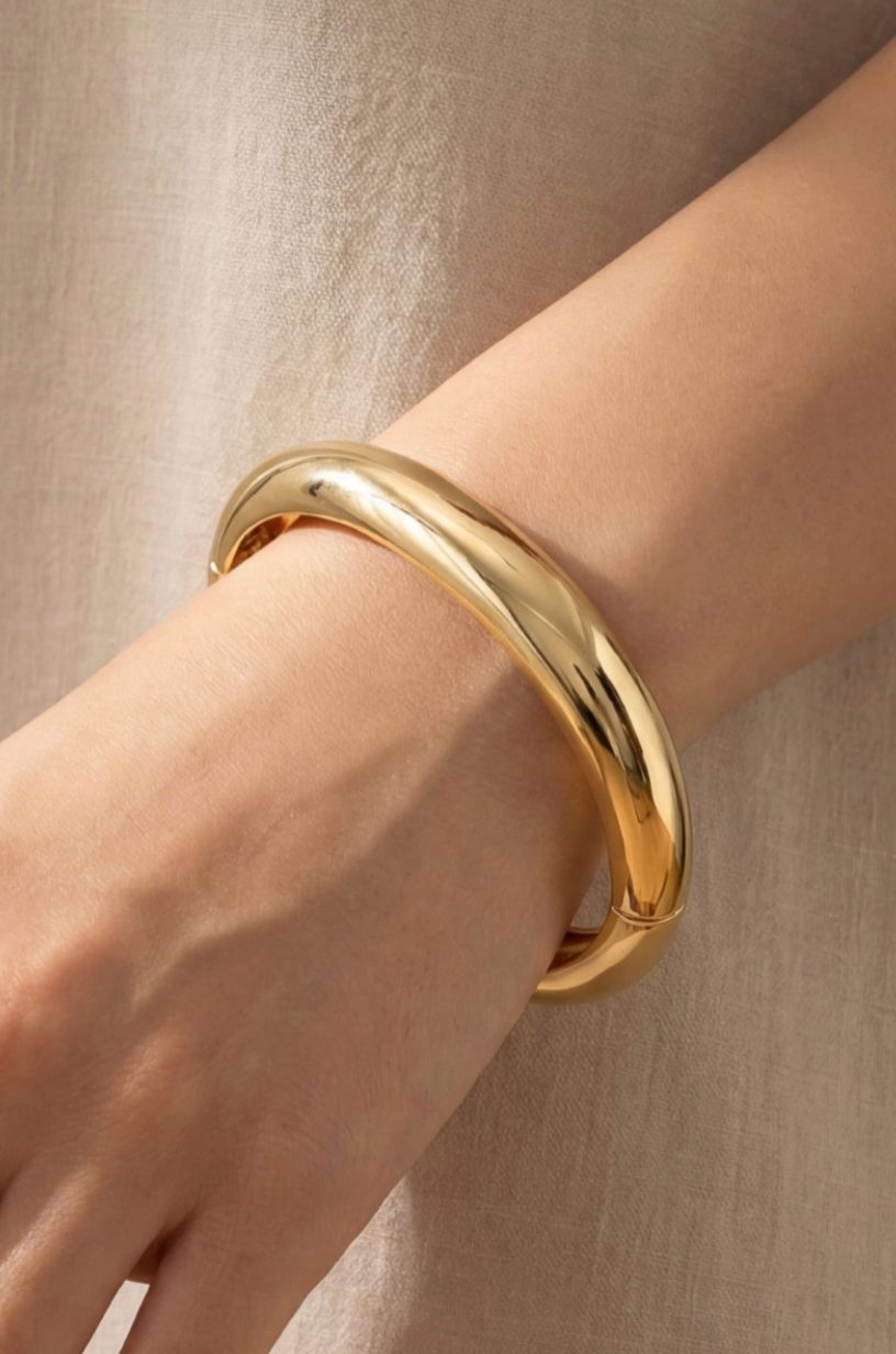 Gold bracelet on a wrist against a neutral background