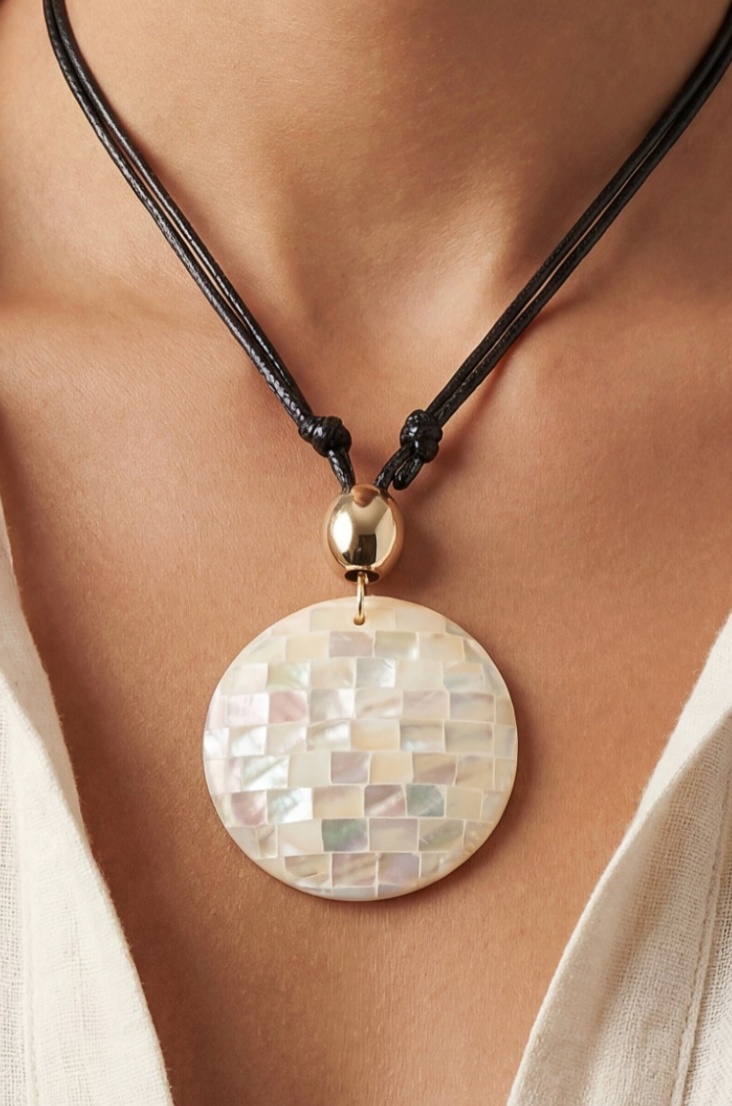 Necklace with a round, mother-of-pearl pendant on a person wearing a white shirt.
