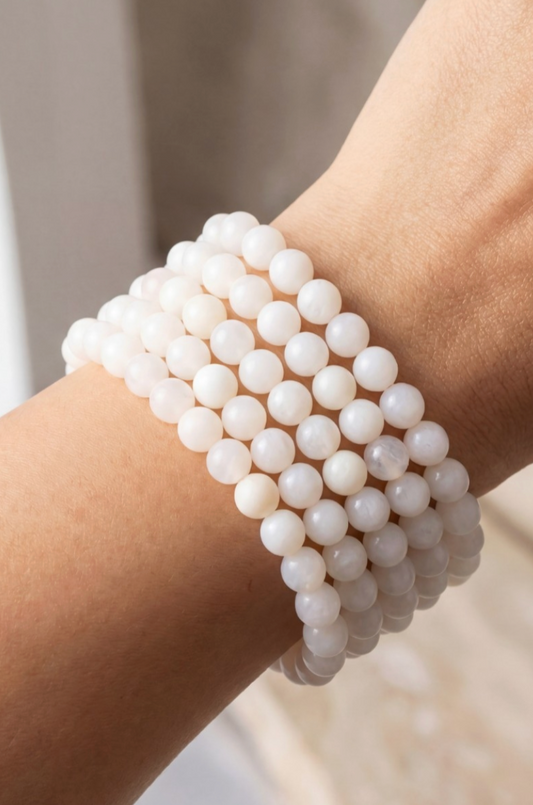 Close-up of a wrist wearing multiple white beaded bracelets against a neutral background