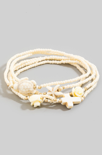 White beaded bracelet with floral and shell designs on a gray background