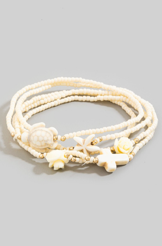 White beaded bracelet with floral and shell designs on a gray background
