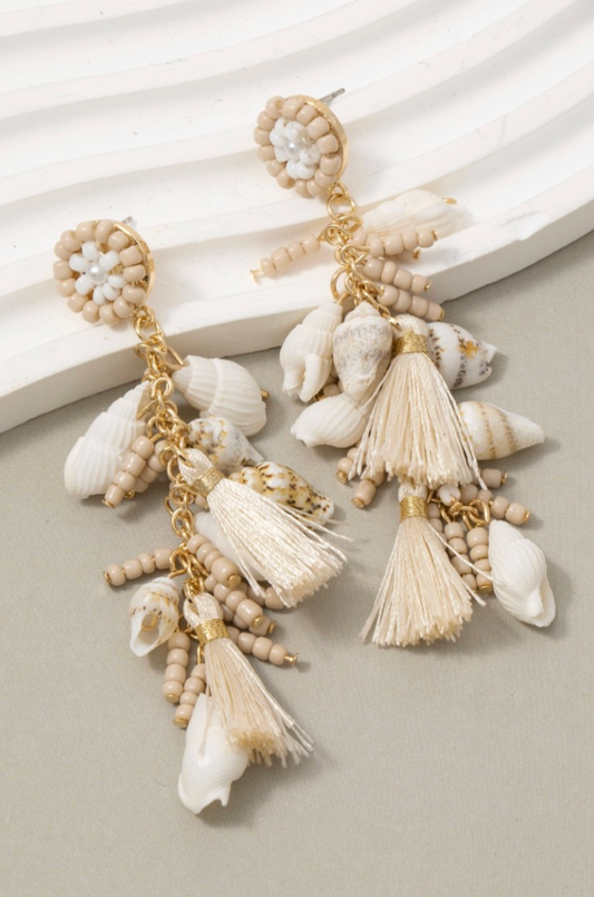 Beige and gold earrings with shell and tassel details on a light background
