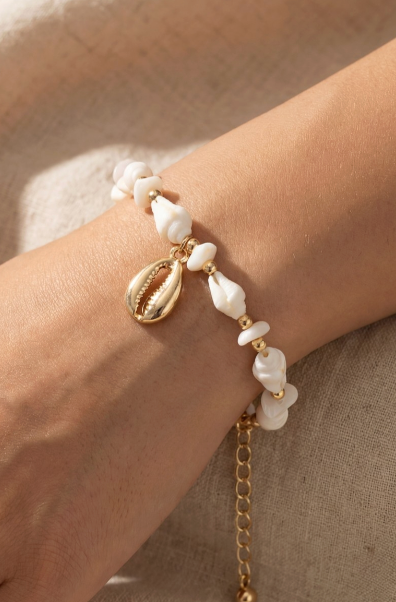Bracelet with pearls and gold chain on a wrist against a neutral background