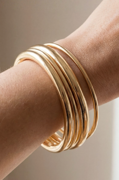 Gold bangles on a person's wrist against a neutral background