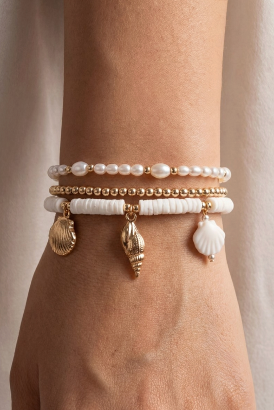Stack of pearl and shell bracelet on a wrist against a neutral background