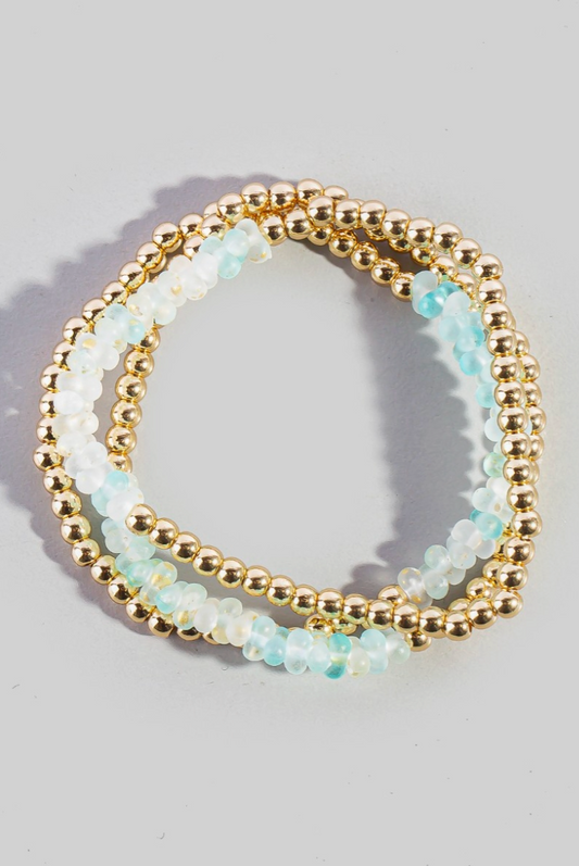 Two beaded bracelets with gold and light blue beads on a gray background