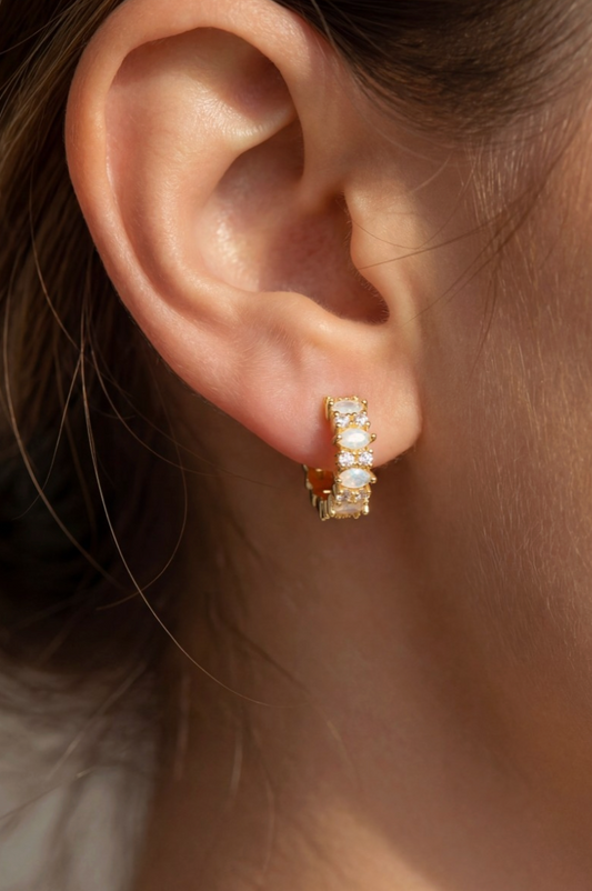 Close-up of an ear wearing a gold hoop earring with clear stones.