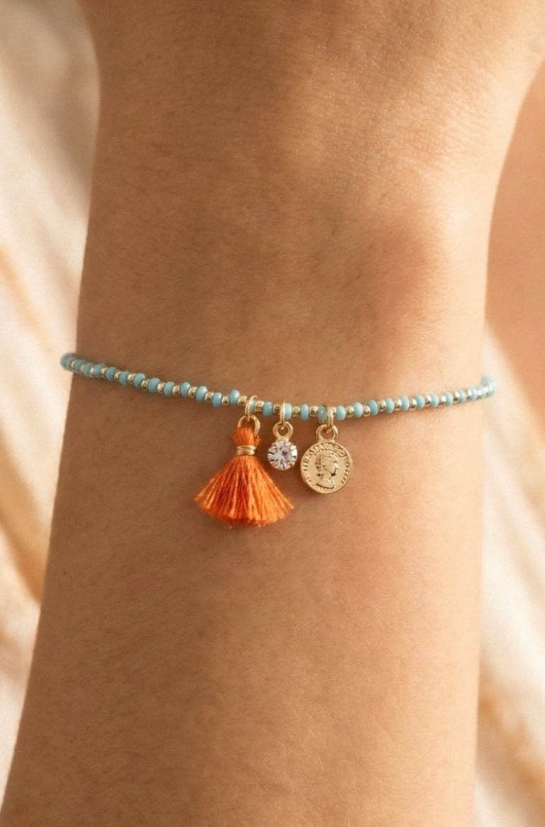 Bracelet with tassel and coin charm on wrist against a neutral background