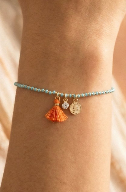 Bracelet with tassel and coin charm on wrist against a neutral background