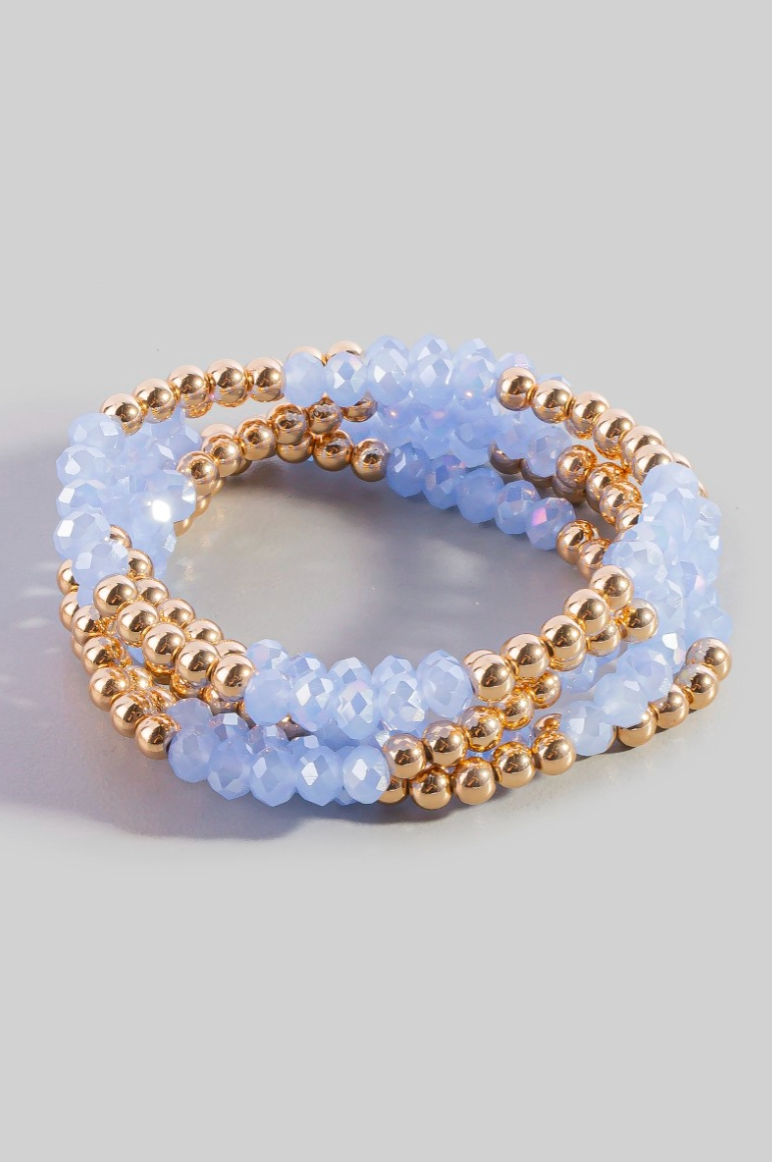 Stack of blue beaded bracelets with gold accents on a light gray background