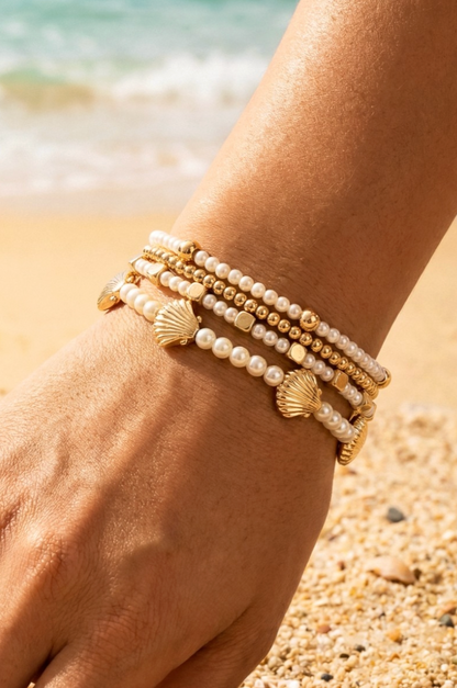 Stack of pearl and gold bracelets on a wrist with a beach background