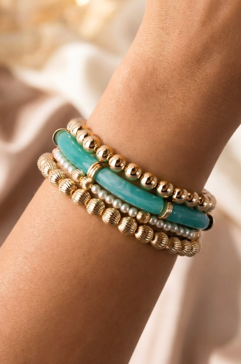 Stack of gold and turquoise beaded bracelets on a wrist with a blurred natural background