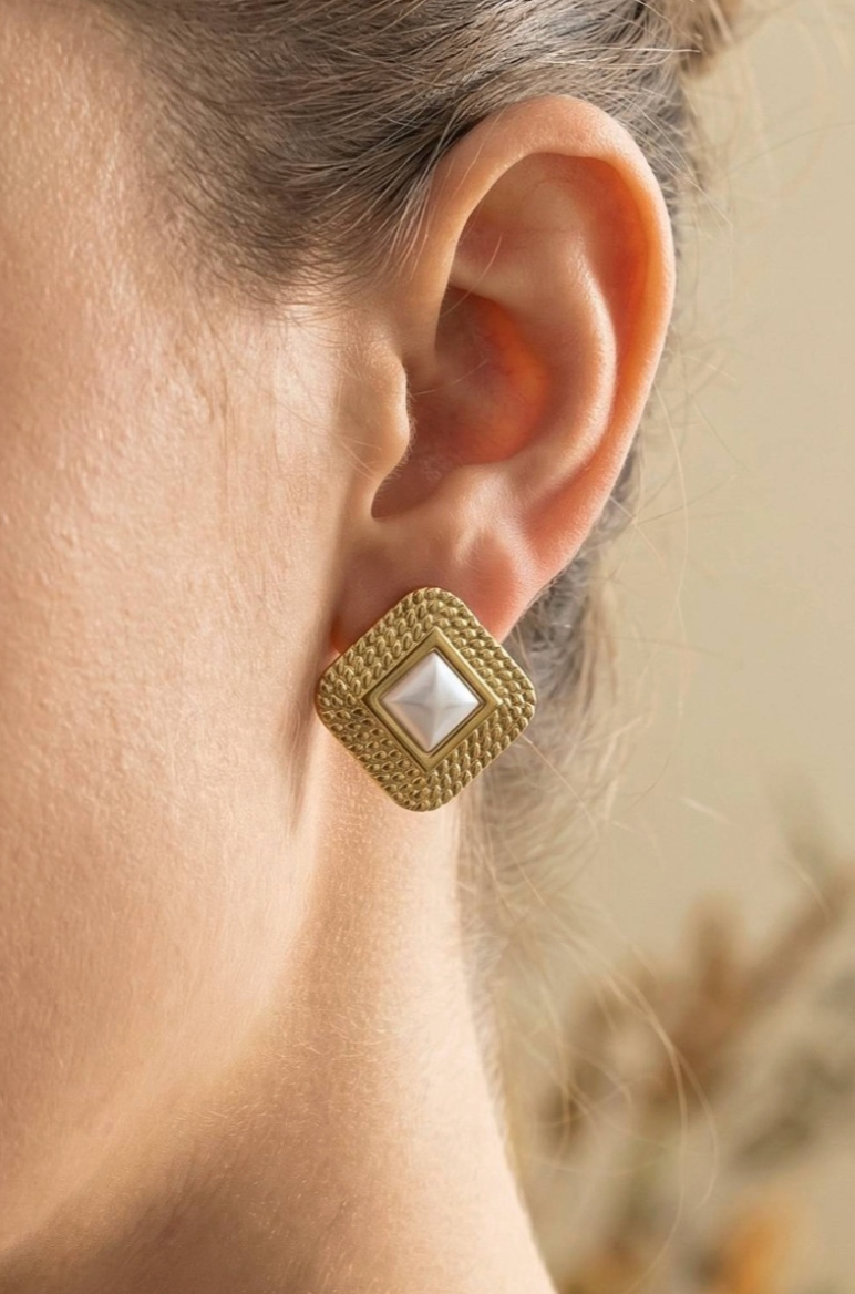 Gold earring with a central gemstone worn by a person