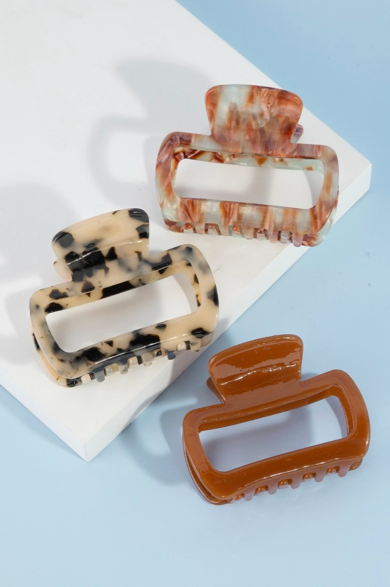 Three tortoiseshell and brown hair clips on a white square pad with a light blue background.