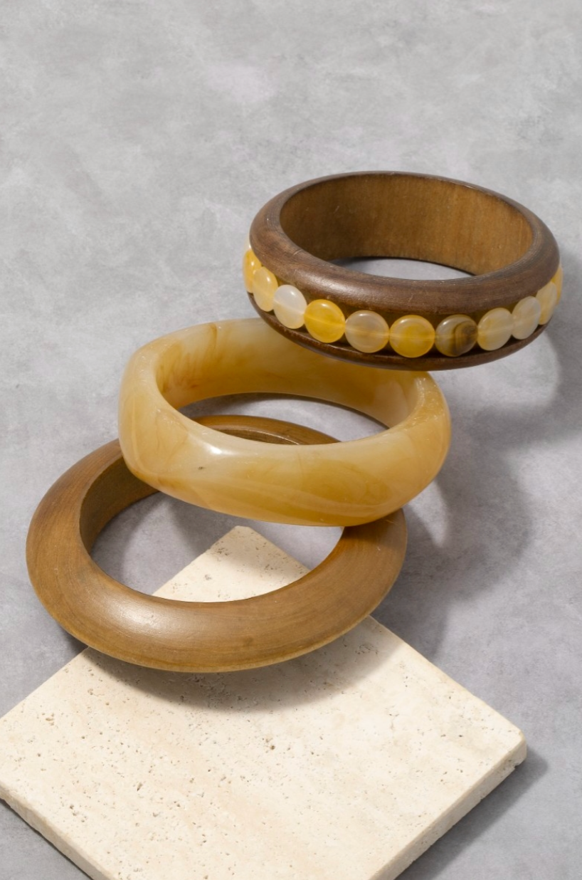 Three wooden bangles stacked on a textured surface with a gray background