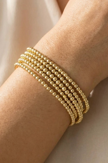 Gold beaded bracelet set on a wrist with a neutral background