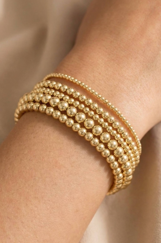 Gold beaded bracelet on a wrist against a neutral background