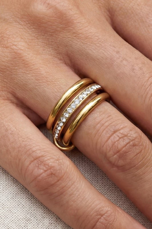 Close-up of a hand wearing two gold rings with diamond accents on a neutral background