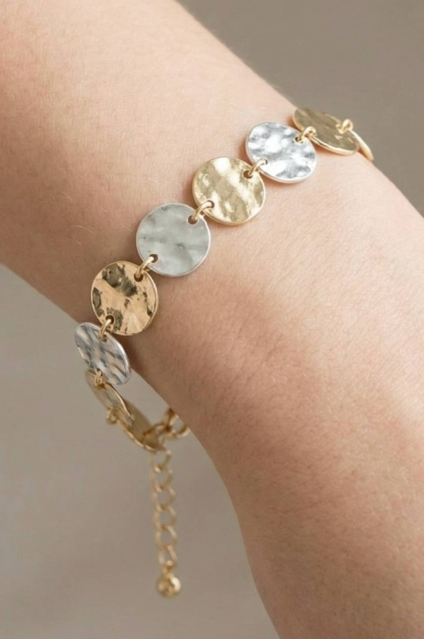Gold and silver bracelet on a wrist against a neutral background