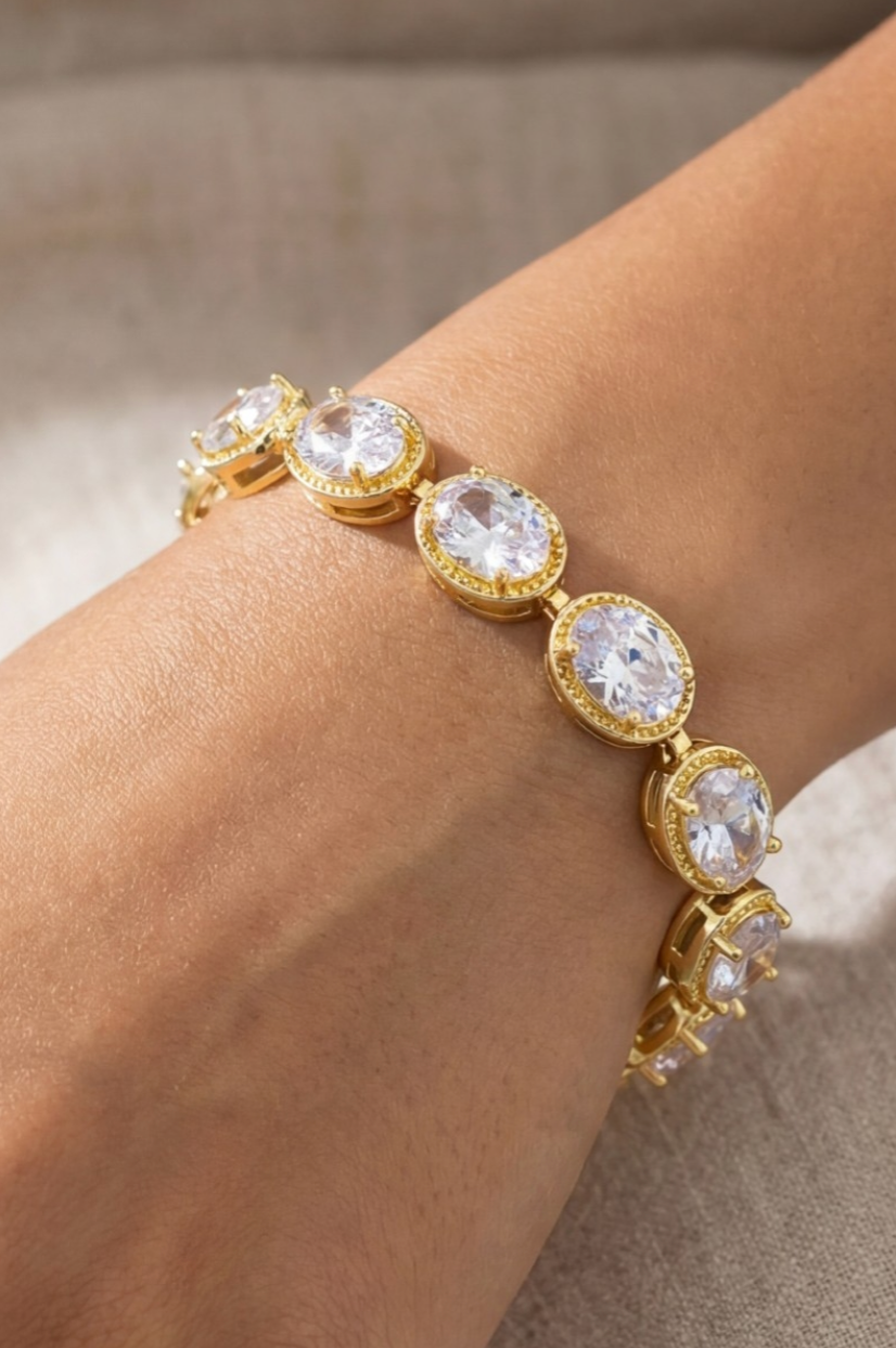 Gold bracelet with clear gemstones on a wrist against a neutral background