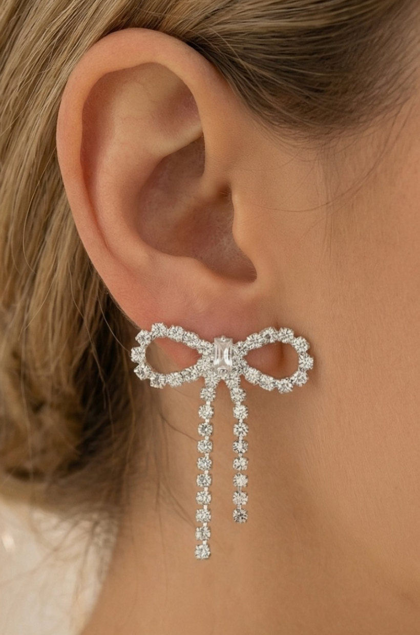 Silver bow-shaped earring worn on an ear with a blurred background