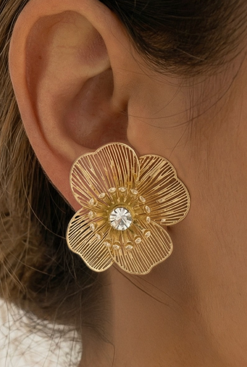 Gold floral earring with a central gemstone worn on an ear.