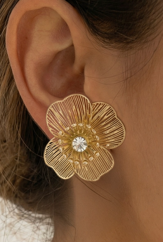 Gold floral earring with a central gemstone worn on an ear.